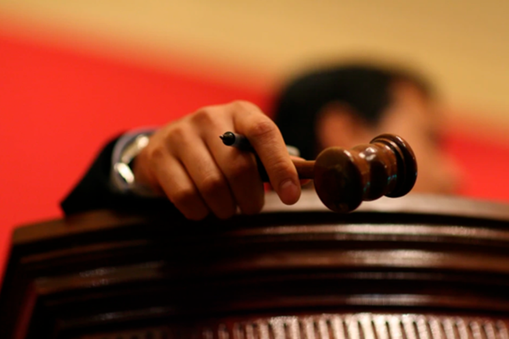 A close-up image of a hand holding a gavel above a wooden podium, with a blurred background.