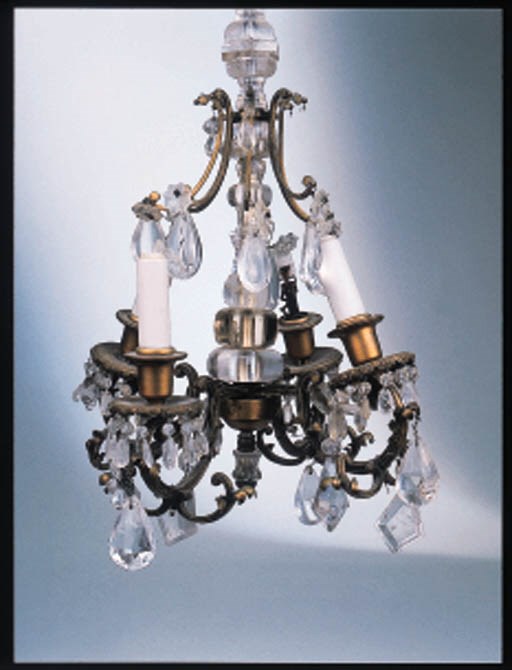 A ROCOCO STYLE GOLD-PAINTED METAL AND CUT-GLASS FOUR-LIGHT CHANDELIER With a panelled multi-baluster-form knop stem issuing scrolled arms decorated with leaves and suspending lusters.