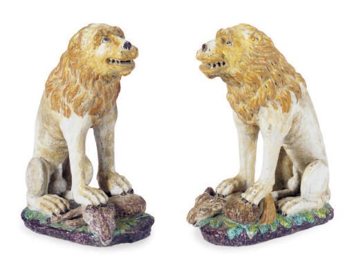 A PAIR OF TIN-GLAZED EARTHENWARE MODELS OF SEATIED LIONS WITH PREY,