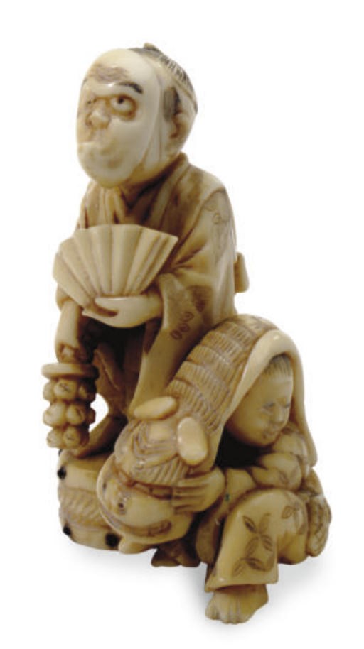 A JAPANESE IVORY NETSUKE OF A MASKED FATHER AND HIS SON UNDER A LION COSTUME,