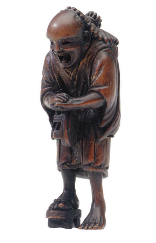 A JAPANESE WOOD NETSUKE OF A MAN HOLDING A SANDAL,