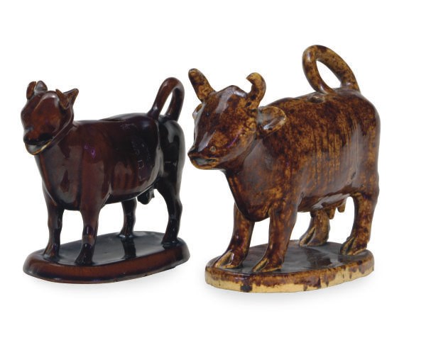 TWO TREACLE GLAZED POTTERY COW-FORM CREAMERS,