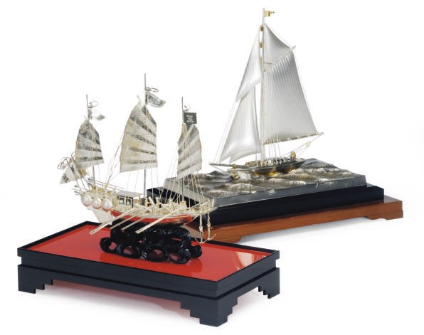 A SILVER MODEL OF A SAILBOAT MOUNTED ON A SILVERED-METAL AND WOOD BASE AND A SILVER MODEL OF A CHINESE OF A JUNK MOUNTED ON A CARVED WOOD BASE,