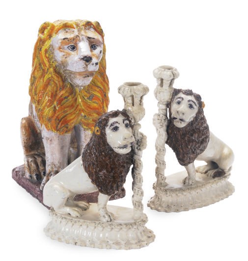 A PAIR OF CONTINENTAL EARTHENWARE MODELS OF SEATED LIONS AS CANDLESTICKS AND A PAINTED TERRACOTTA MODEL OF A LION,
