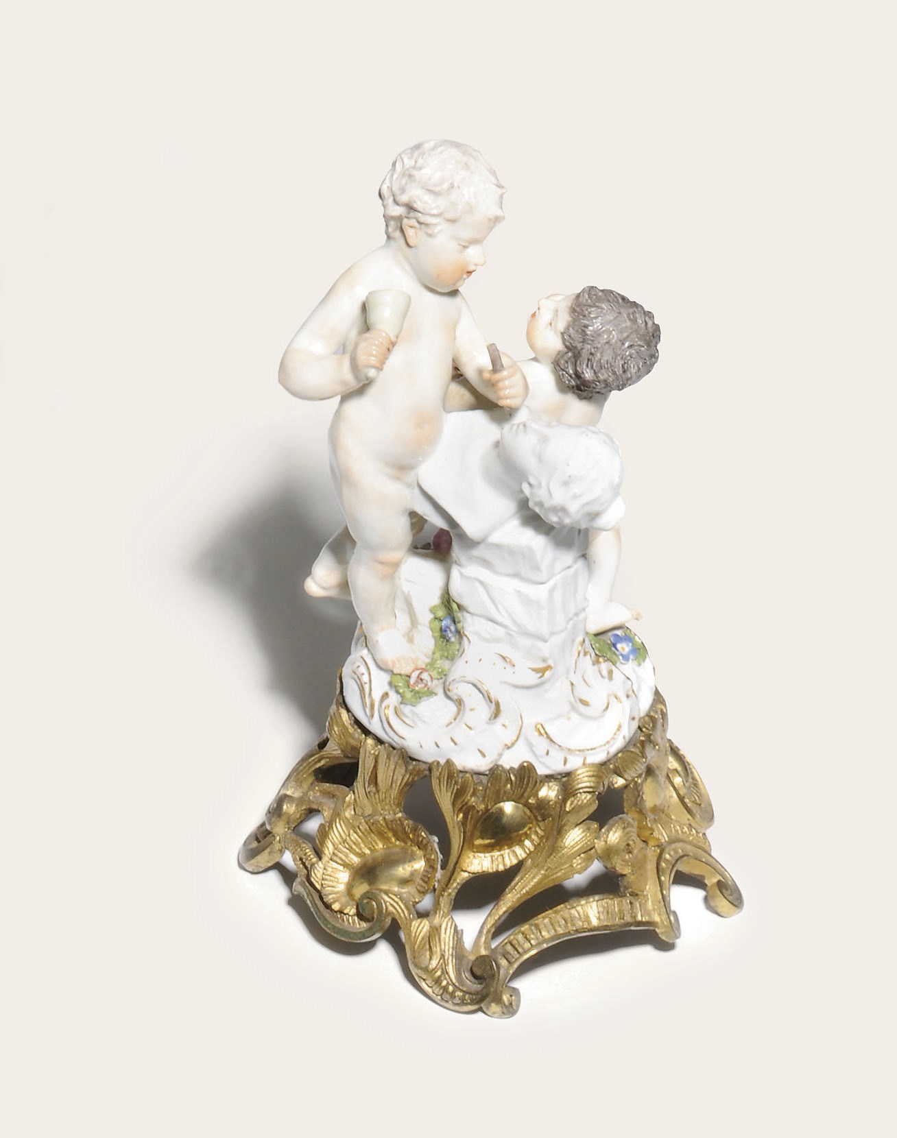 A MEISSEN PORCELAIN GILT-METAL MOUNTED GROUP OF PUTTI EMBLEMATIC OF PAINTING AND SCULPTURE